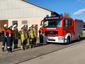 eine Gruppe von acht Feuerwehrleuten steht angetreten vor einem Löschfahrzeug