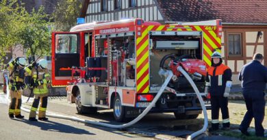 der Maschinist steht hinter dem Feuerwehrfahrzeug und bedient die Pumpe, während sich ein Trupp neben dem Fahrzeug mit Atemschutz ausrüstet.