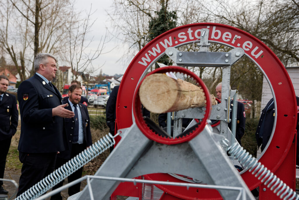 Kreisbrandmeister Raimund Großberger erklärt den Kommandanten den neuen Holzspannungssimulator vor der Frankenlandhalle in Schnelldorf.