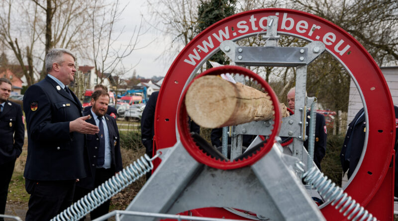 Kreisbrandmeister Raimund Großberger erklärt den Kommandanten den neuen Holzspannungssimulator vor der Frankenlandhalle in Schnelldorf.